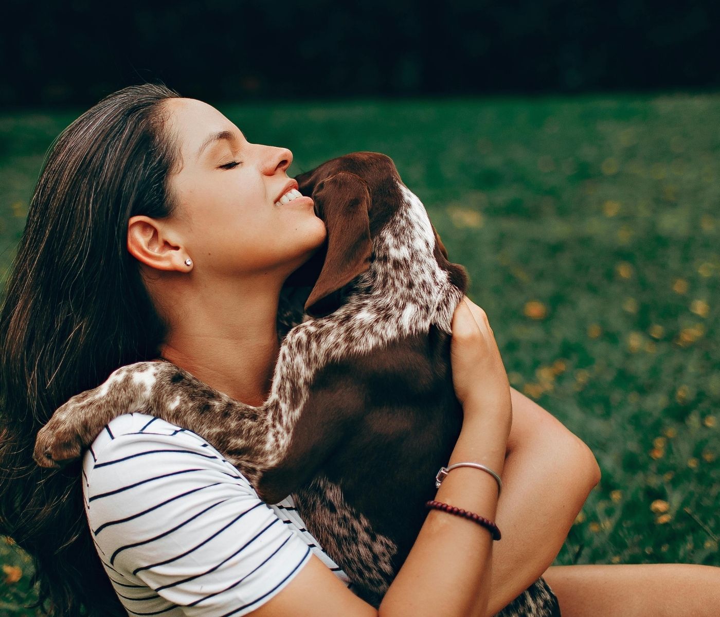 A person embracing a dog while sitting on grass in a park.