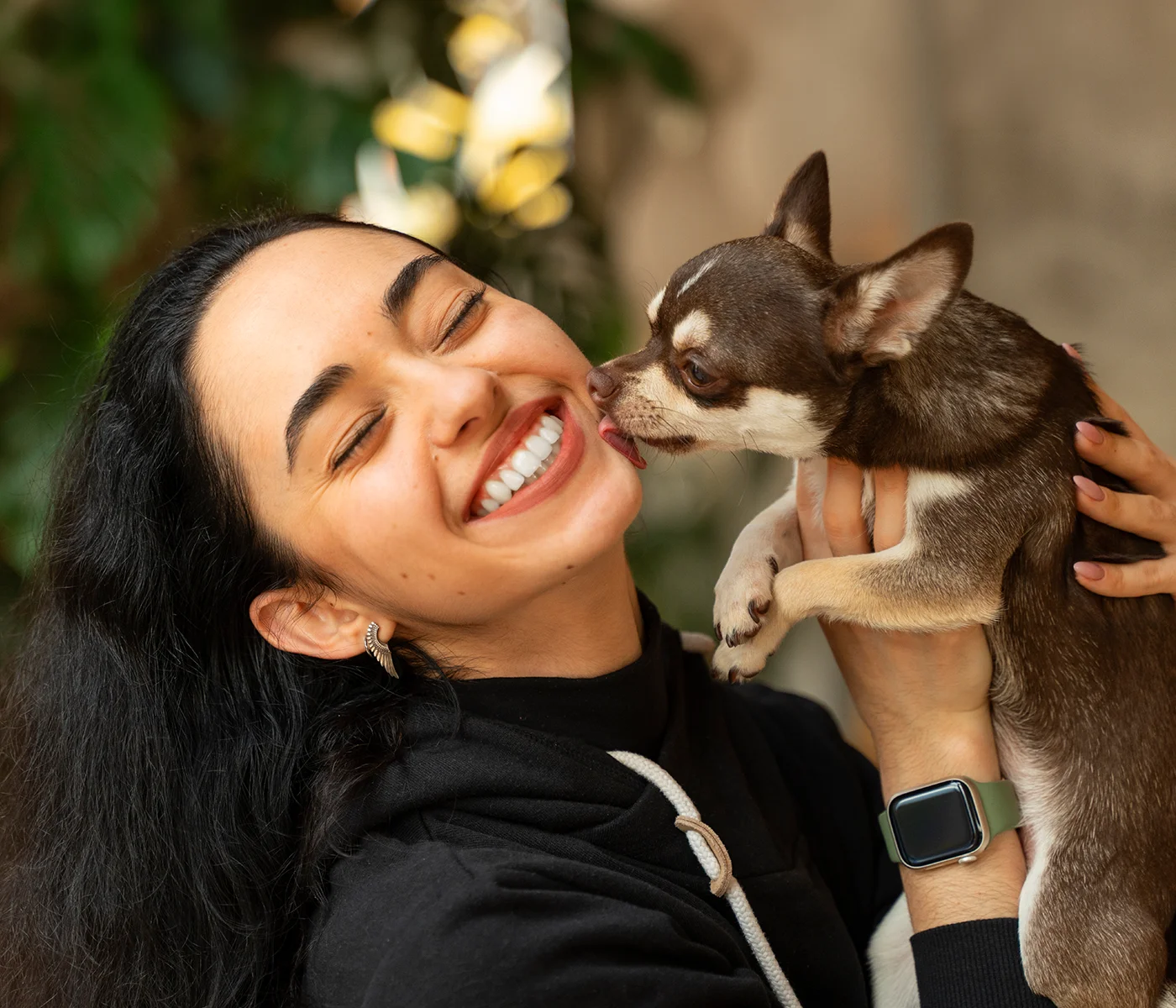 A young woman holds up her small dog and it licks her cheek